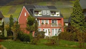 Une maison à deux étages avec une façade rouge, des ornements blancs et un balcon agrémenté de plantes.