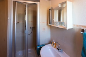 Une salle de bain avec une douche à parois de verre, un lavabo blanc doté d’un distributeur de savon et un miroir au-dessus du lavabo.