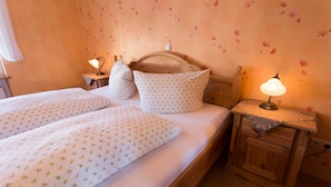 Une chambre à coucher avec un lit en bois, deux oreillers, une table de chevet avec une lampe et un papier peint à motifs floraux.