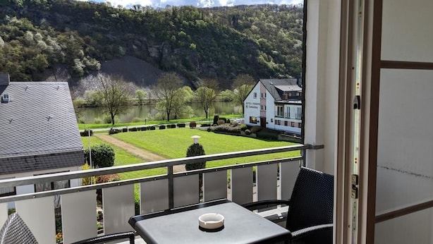 Un balcon avec une table et une chaise, donnant sur un lac et un bâtiment sur lequel on peut lire l’inscription « Hôtel Penzberg & Spa ».
