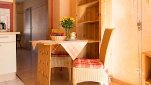Une cuisine chaleureuse avec une table en bois, une chaise en osier et un panier rempli de fruits et de fleurs.