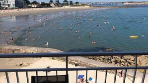 Een strand met mensen die zwemmen en zonnebaden. Achtergrond met gebouwen en bomen.