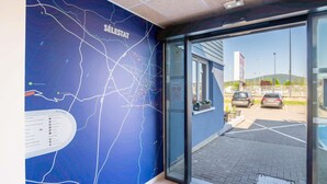 Pared azul com um mapa e a palavra 'SÉLESTAT' escrita, porta de entrada de vidro e um estacionamento com carros.
