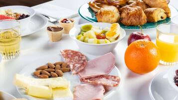 Ein Frühstückstisch mit verschiedenen Speisen, darunter Gebäck, Obst, Käse, Wurst und ein Glas Orangensaft.