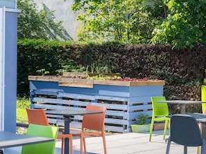 An outdoor seating area with a raised planter bed, tables, and chairs. - Ibis Budget Sélestat (Sélestat)