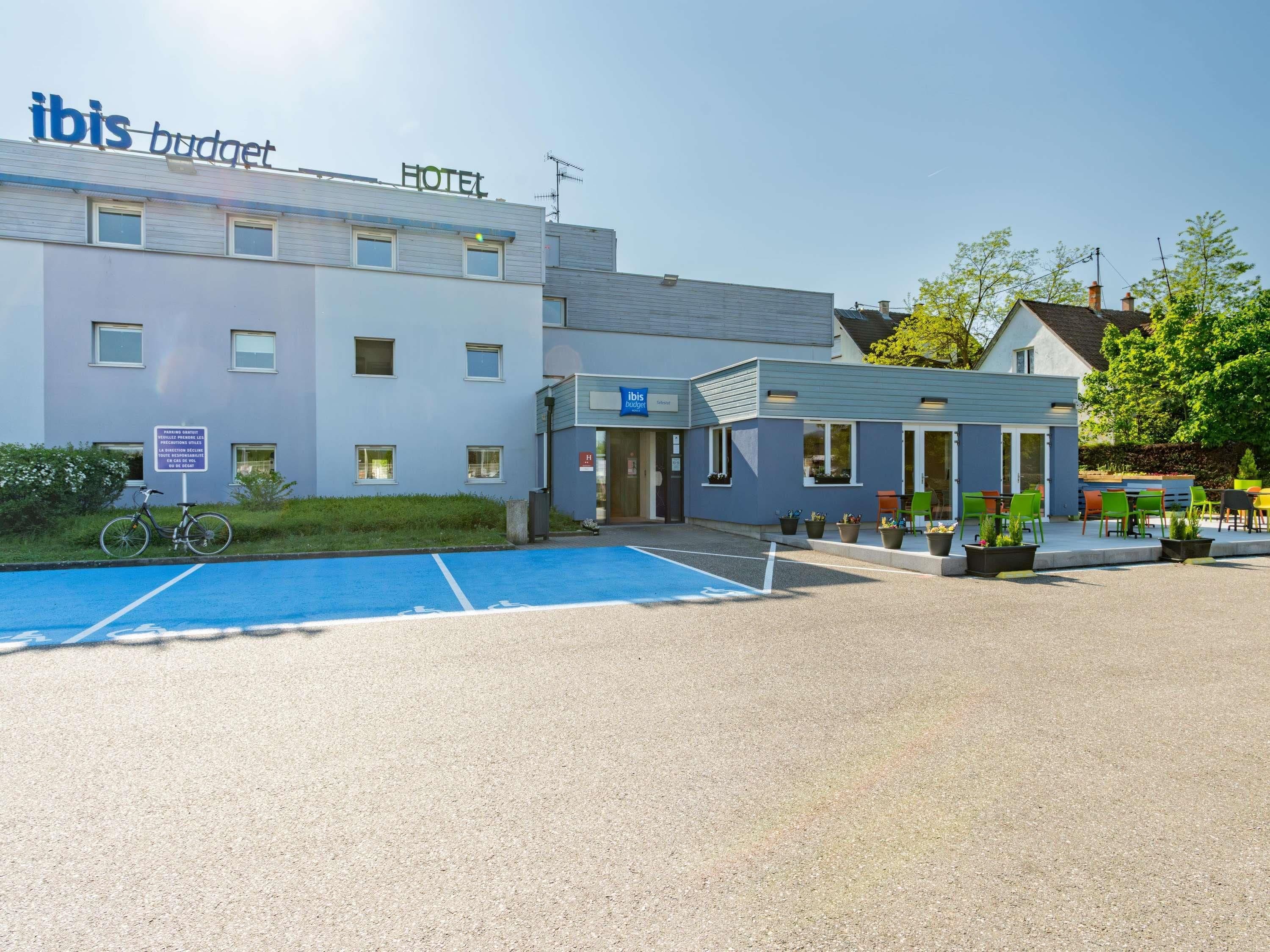 A hotel with a blue and white exterior, a parking area, and outdoor seating.