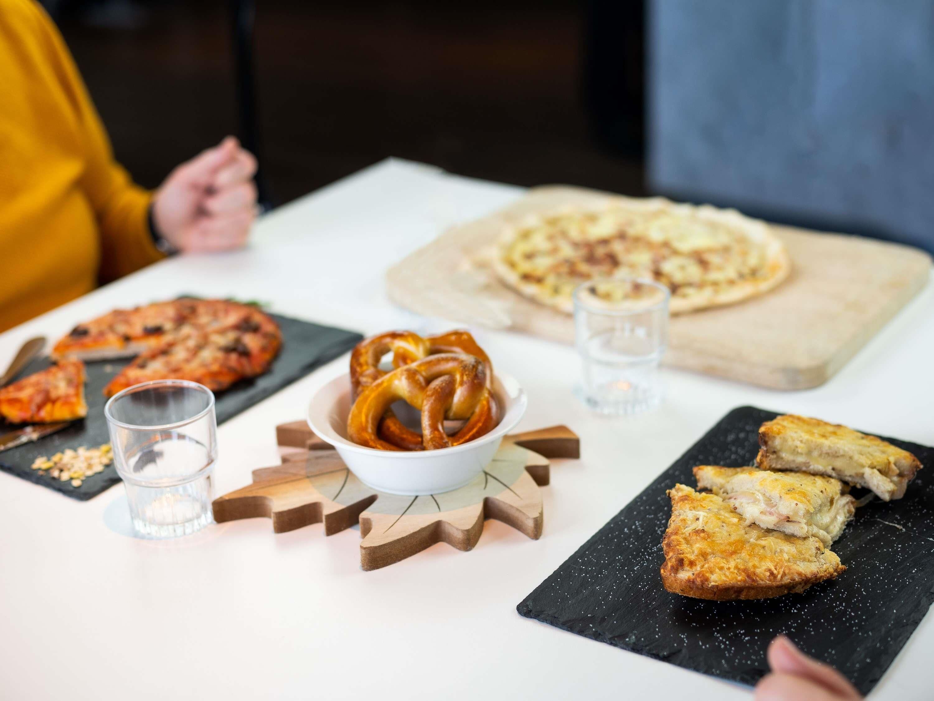 A dining table with various food items, including pizza, pretzels, and bread.