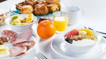 Une table mise pour le petit-déjeuner, avec des assiettes remplies de nourriture, un verre de jus d’orange et une tasse.