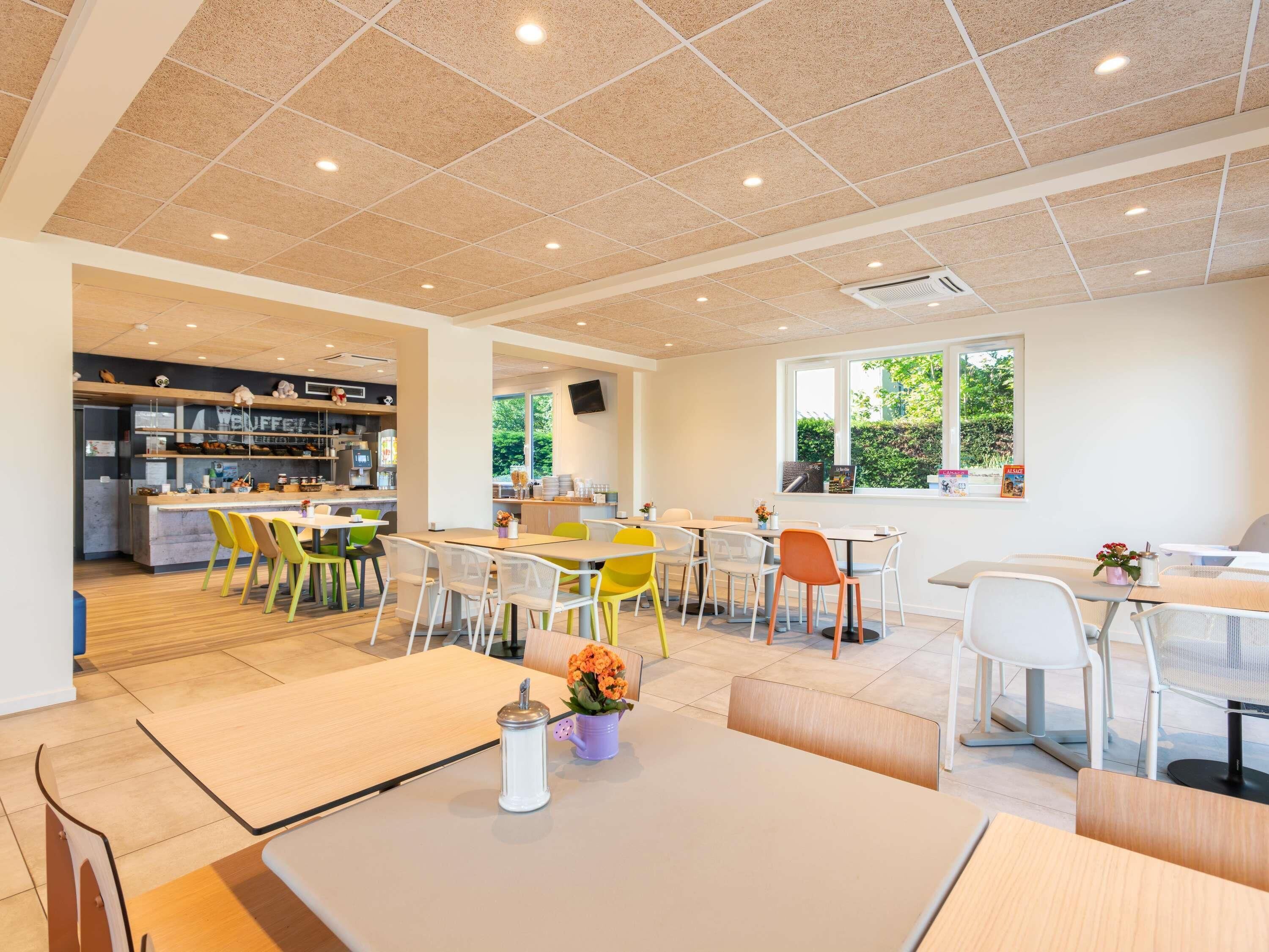 Un espace intérieur spacieux comprenant plusieurs tables et chaises, un coin cuisine et une fenêtre laissant entrer la lumière naturelle.