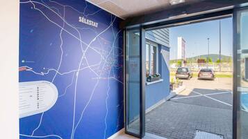 A hotel entrance with a blue wall featuring a map and a glass door leading to a parking area.