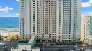 Un hotel de gran altura con varios balcones, un estacionamiento y vista al océano.