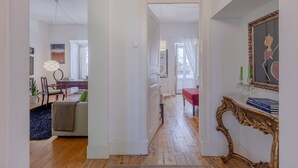 Uma sala de estar ampla com piso de madeira, um sofá, uma mesa de centro e uma mesa de jantar com cadeiras. Há uma escada que leva a outro andar.