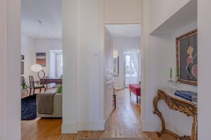 Een ruime woonkamer met houten vloer, een bank, een salontafel en een eettafel met stoelen. Er is een trap die naar een ander niveau leidt.