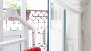 Quarto com piso de madeira, porta e cortina brancos, e toalha vermelha pendurada em um cabide branco.
