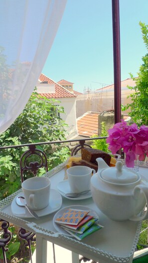 Een balkon met een gedekte tafel voor thee, inclusief kopjes, een theepot en een dienblad met lekkernijen.