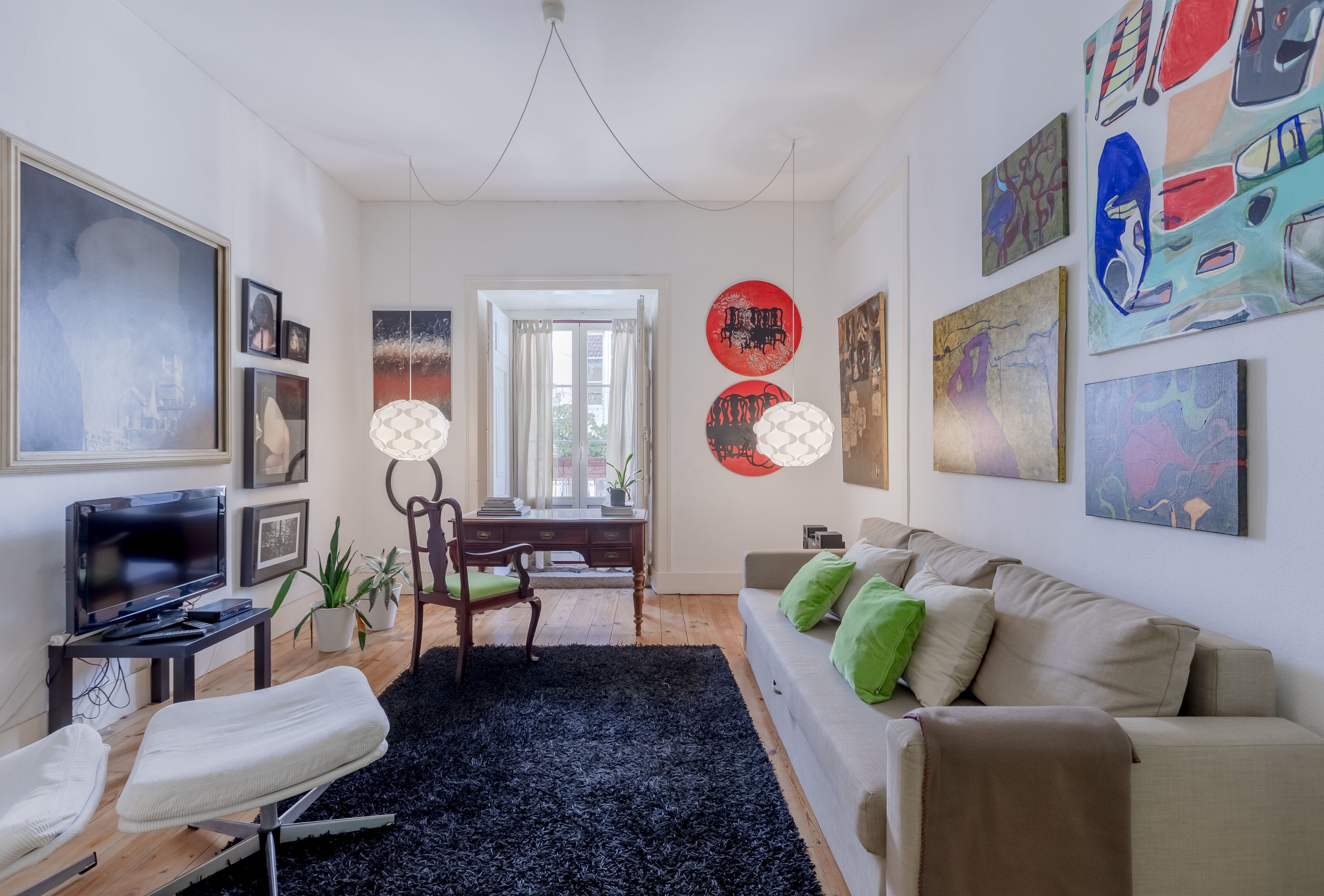 Un salon moderne avec un canapé, un téléviseur, une table à manger avec des chaises et des œuvres d’art accrochées aux murs.