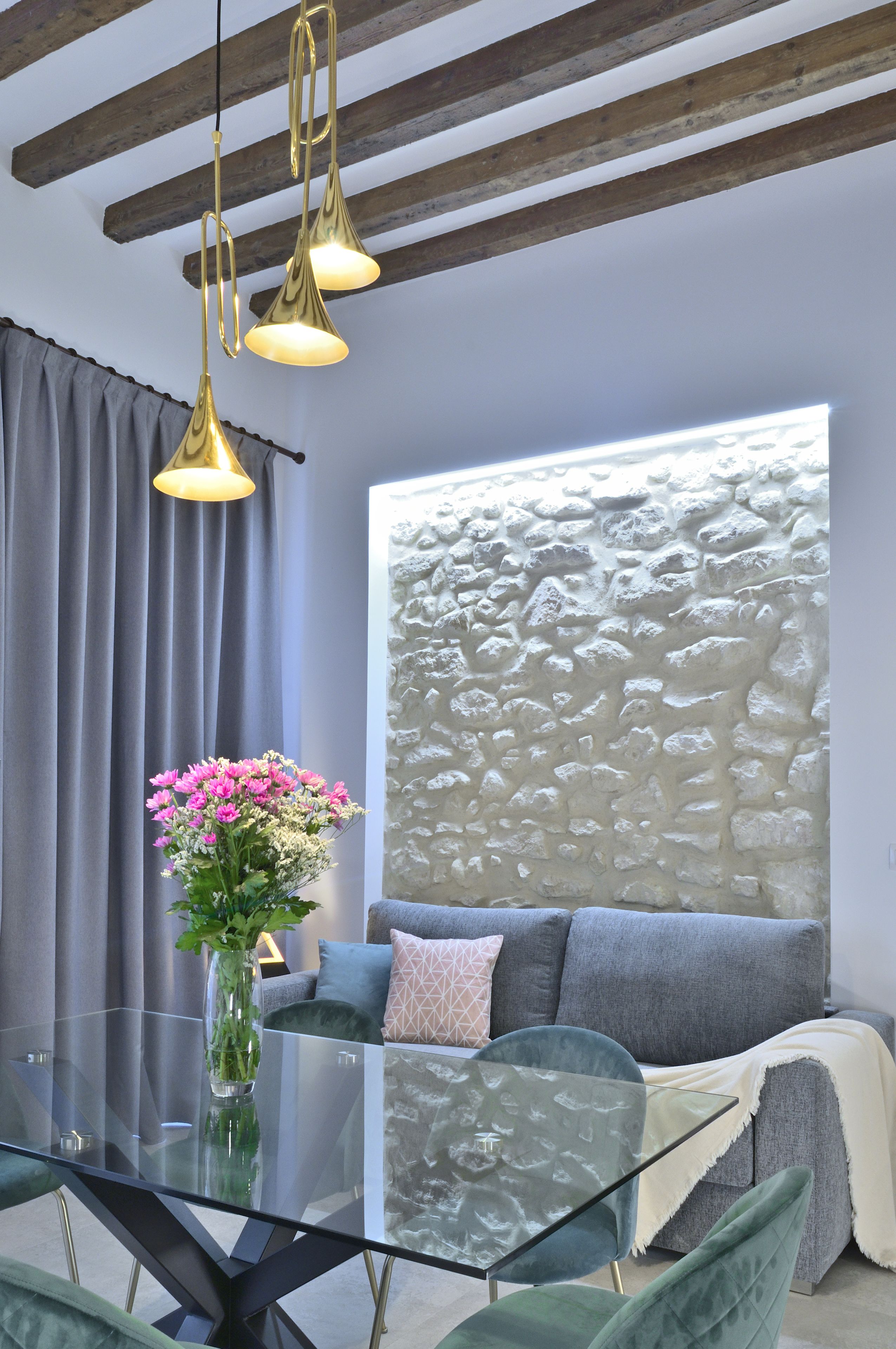 A modern living room with a glass table, a sofa, and a decorative wall.