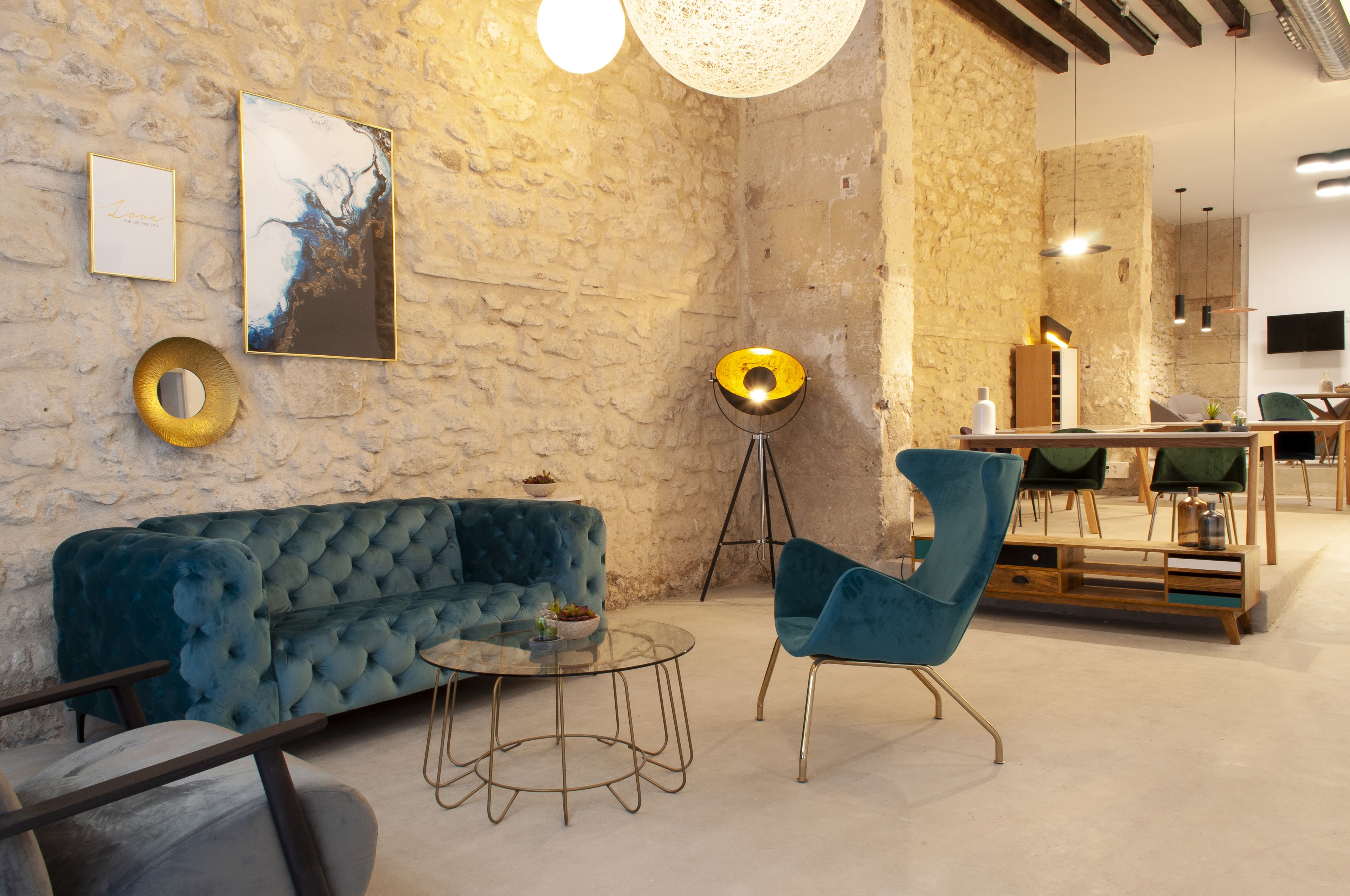 A modern interior with a stone wall, a blue velvet sofa, a glass coffee table, and a blue armchair.