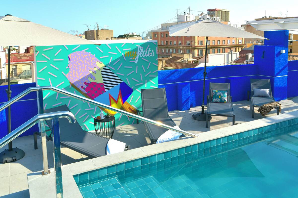 A rooftop pool area with a colorful mural, lounge chairs, and a clear view of the cityscape.
