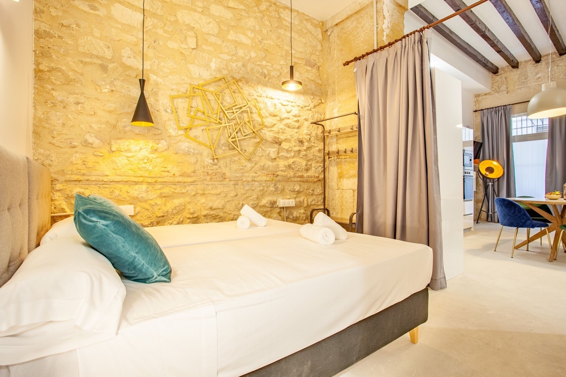 A bedroom with a stone wall, a bed with white linens, a blue pillow, and a hanging light fixture.