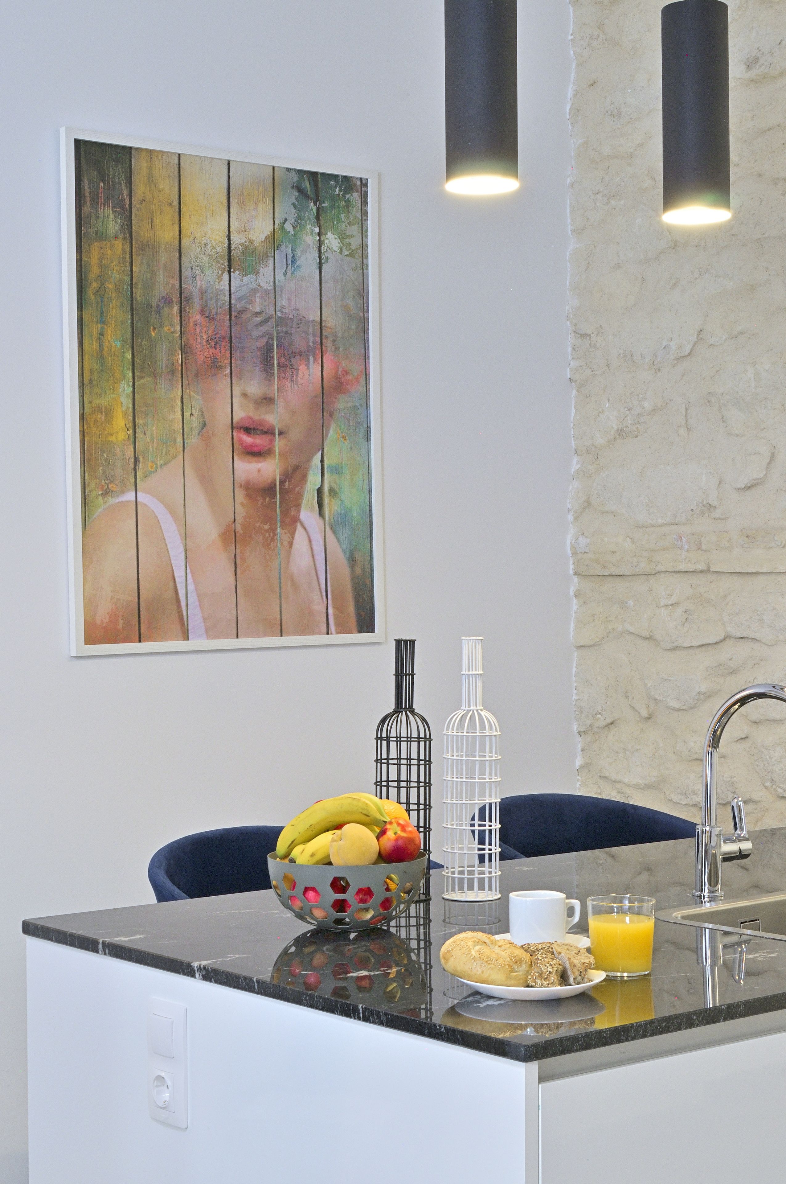 A modern kitchen with a marble countertop, a bowl of fruit, a white mug, and a glass of orange juice.