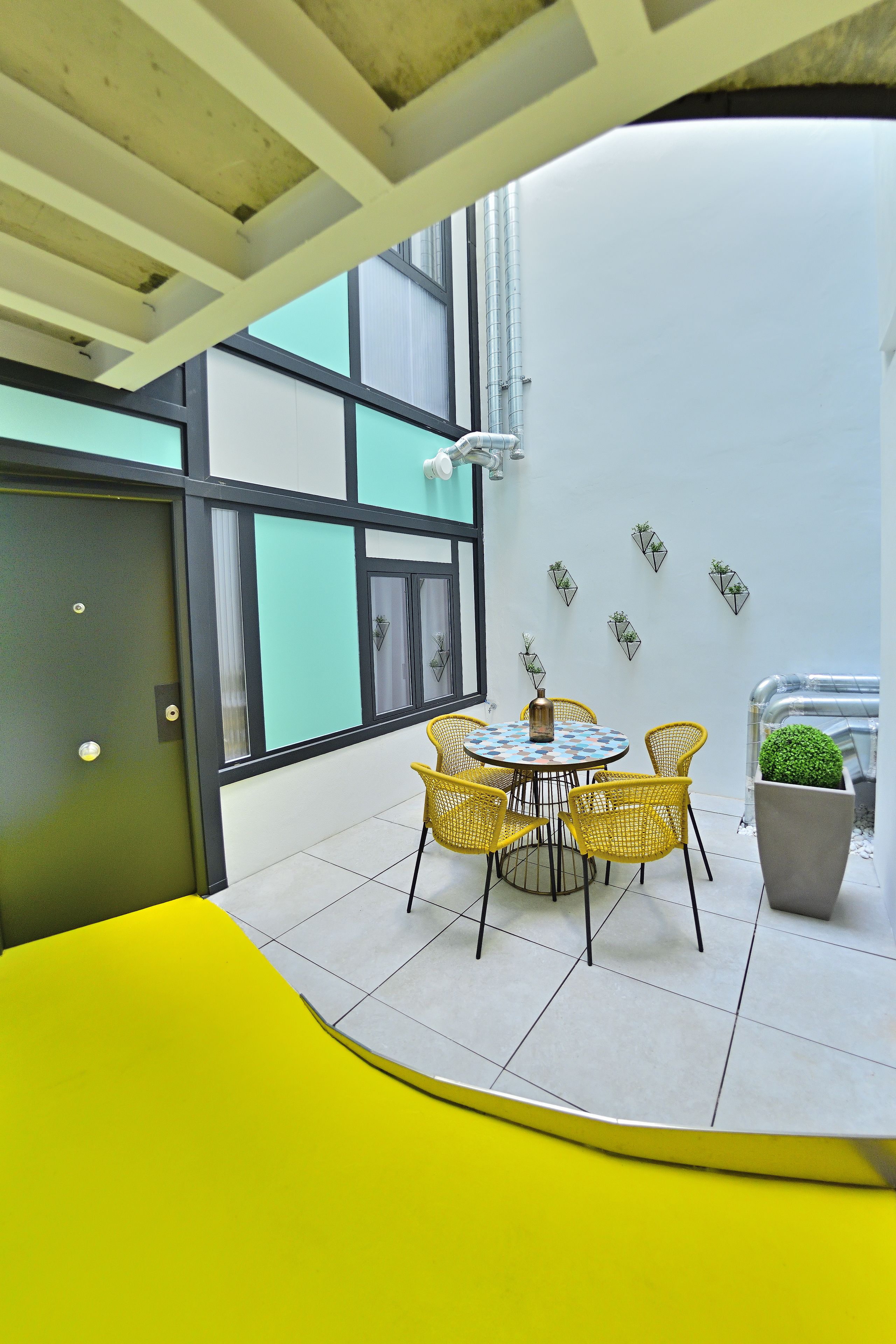 A modern indoor space with a yellow curved bench, a round table with chairs, and potted plants.
