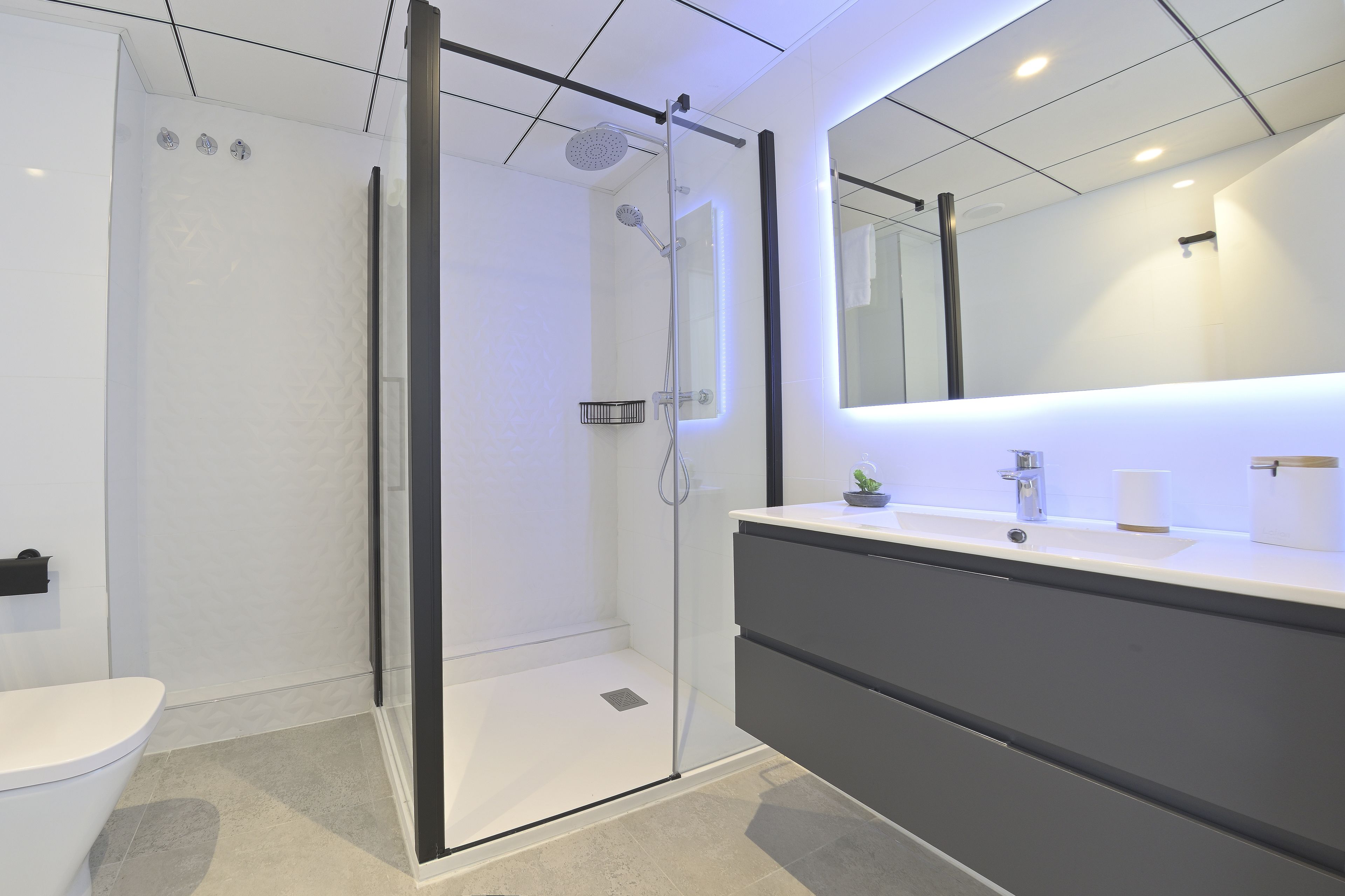 Une salle de bain moderne avec une douche à parois de verre, un lavabo blanc avec un miroir et un meuble-lavabo aux tons foncés.