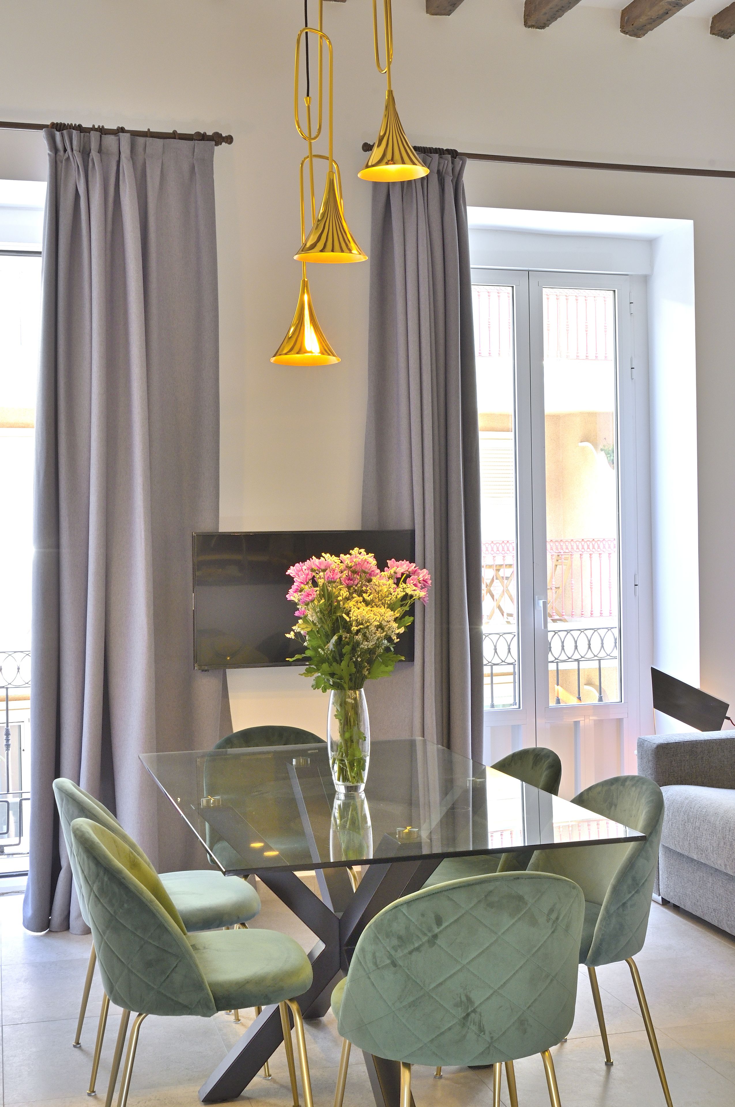 Een moderne eetruimte met een glazen tafel, groene beklede stoelen en een bloevas.