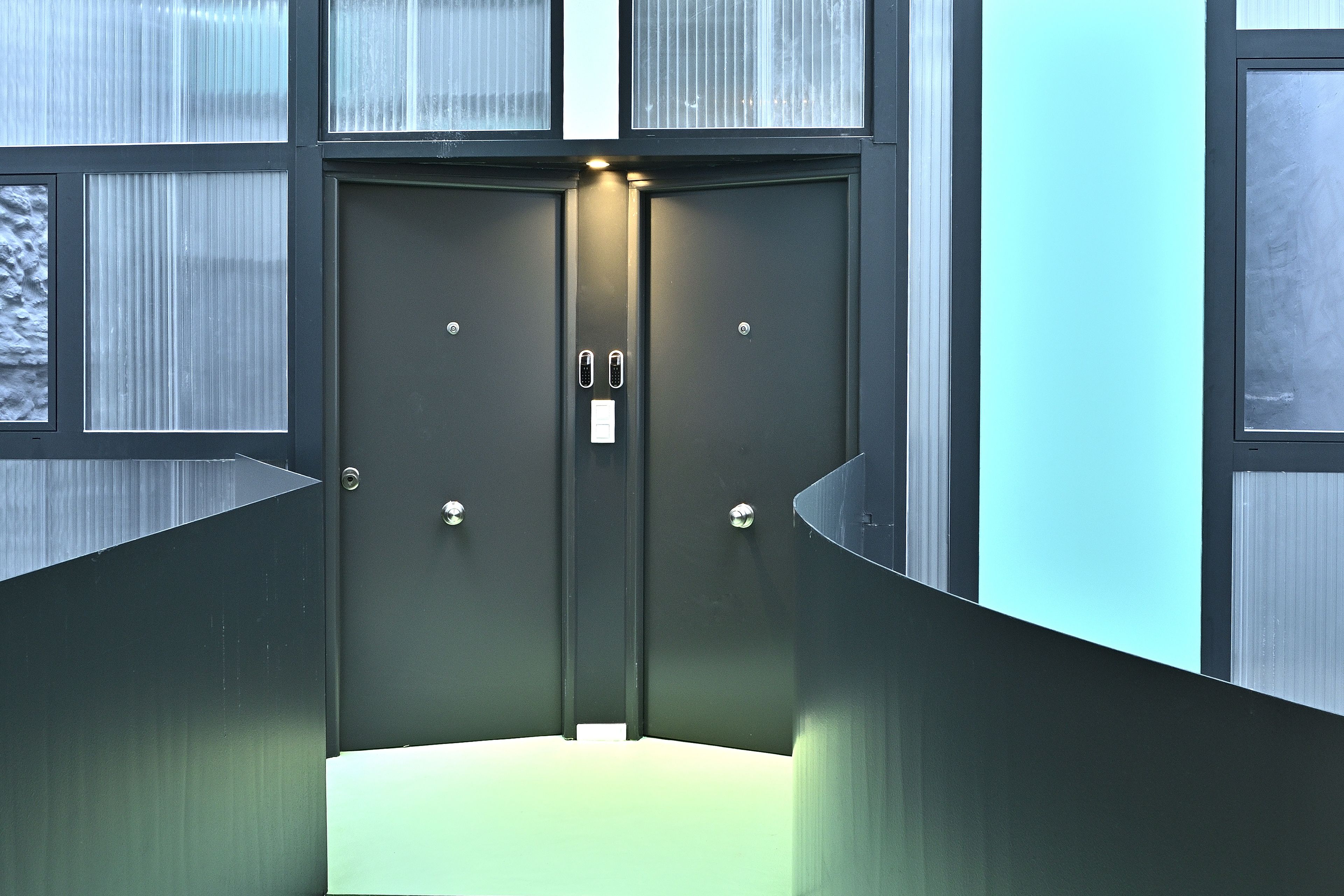 Un ascensor moderno con detalles metálicos, paneles de vidrio y una lámpara sobre las puertas.