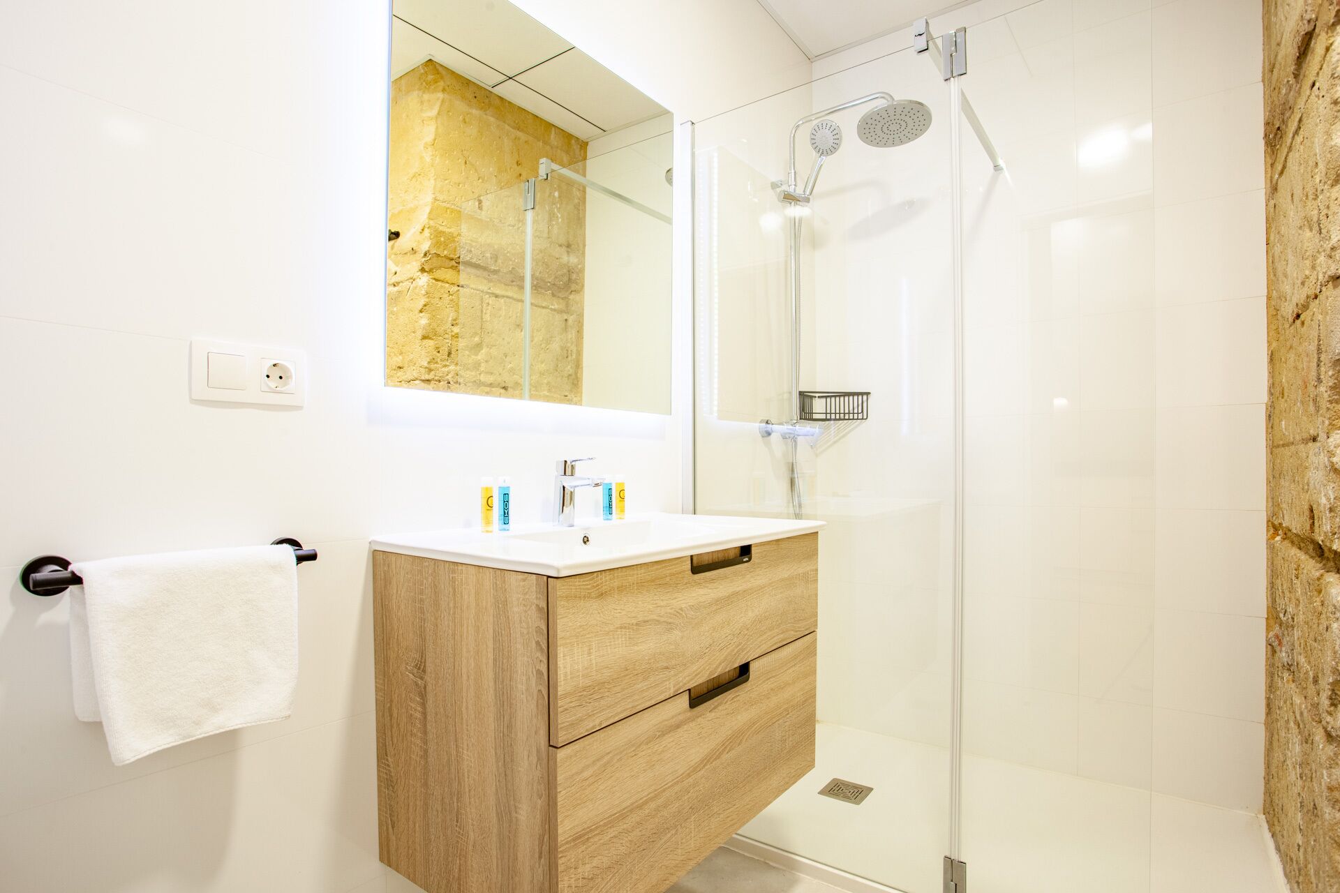 Ein modernes Badezimmer mit einem Holzwaschtisch, einer Duschkabine aus Glas und einem großen Spiegel.