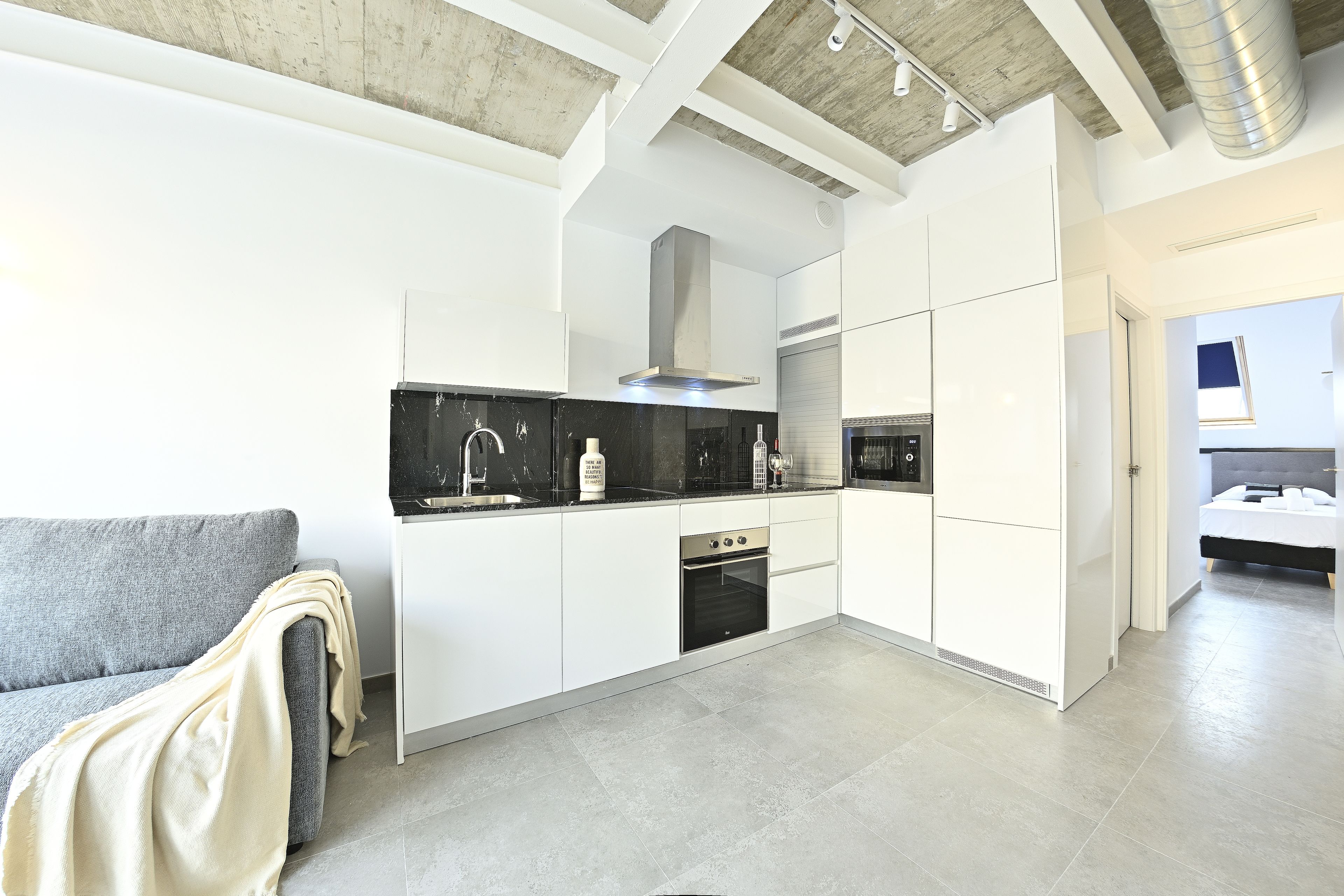 Una cucina moderna con mobili bianchi, un divano grigio e un'ampia finestra.