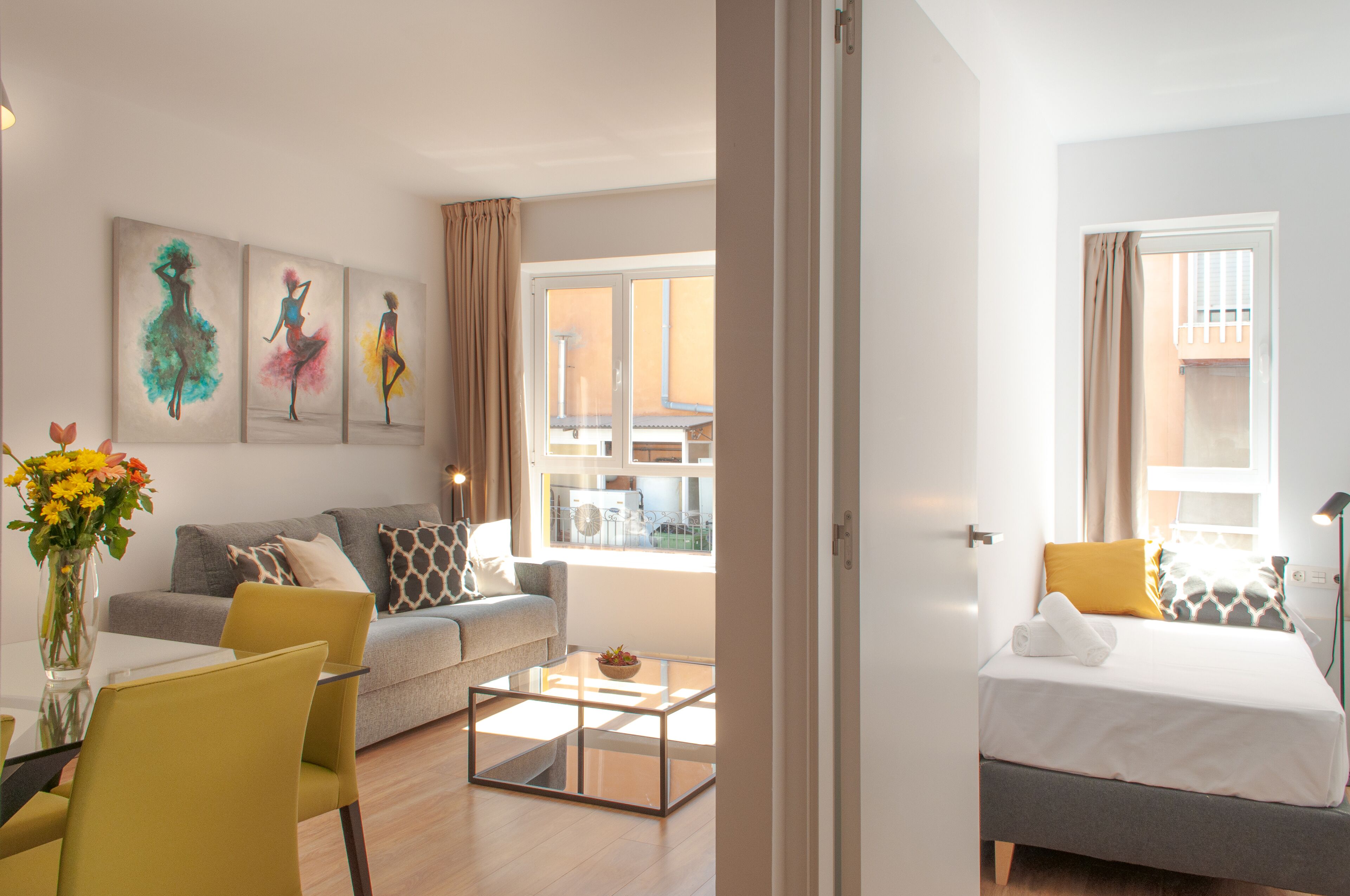 Et moderne hotelværelse med sofa, glasbord, seng med en foldet håndklæde og et kunstværk på væggen.