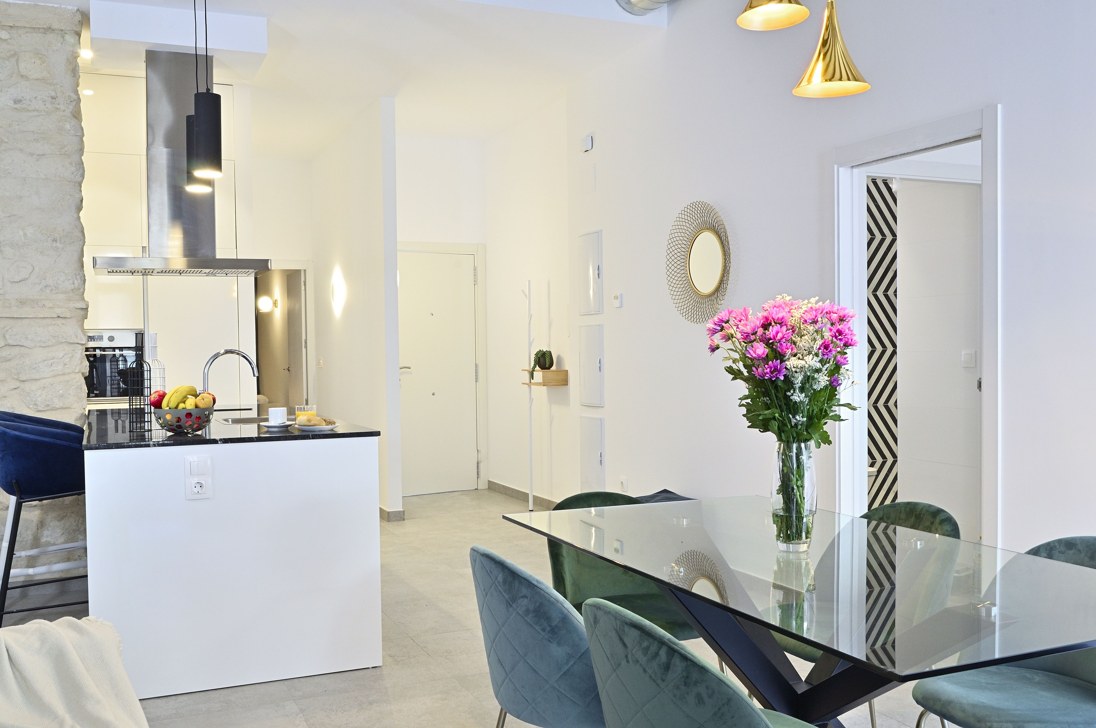 Une cuisine moderne avec des meubles blancs, un îlot central et un coin repas comprenant une table en verre et des chaises bleues.
