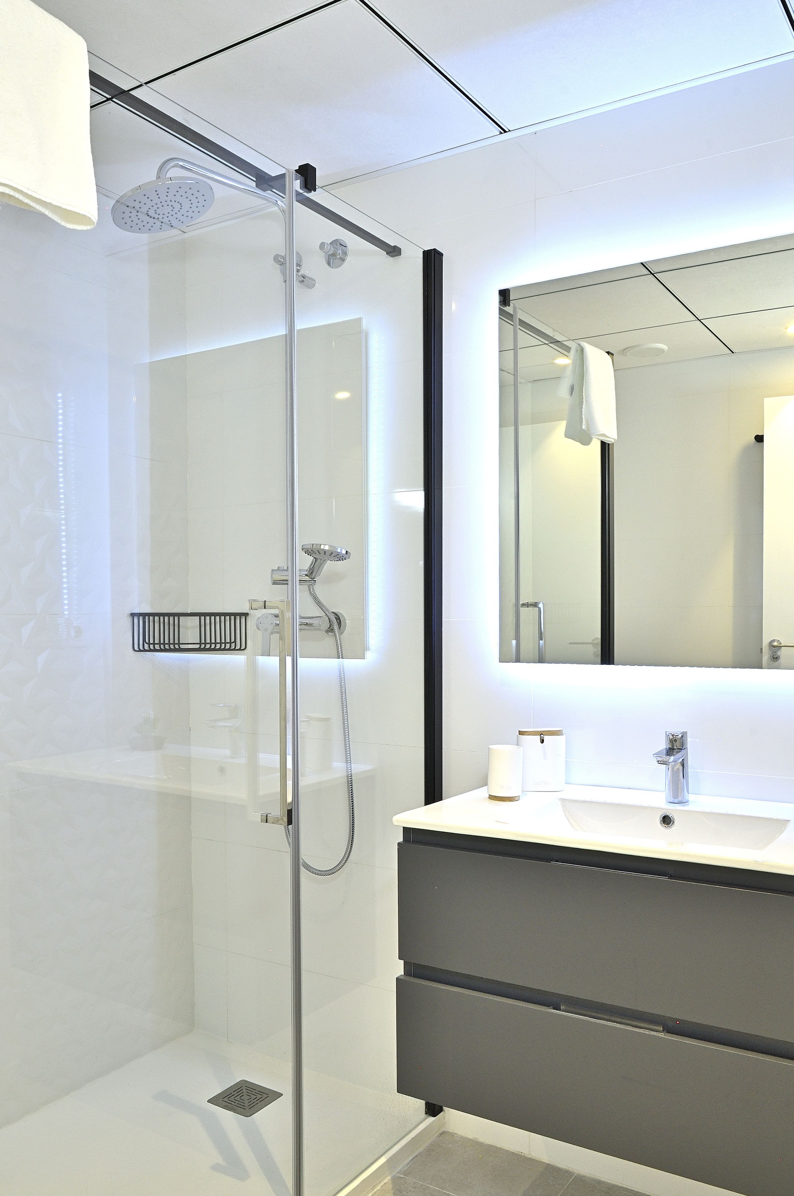 A modern bathroom with a glass-enclosed shower, a large mirror, and a dark-toned vanity.