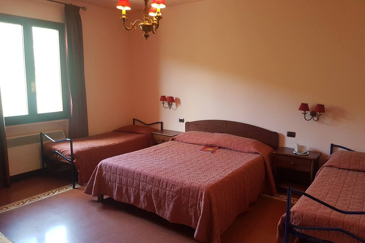 Una habitación con dos camas individuales, una cama doble, un calentador, un teléfono y una araña.