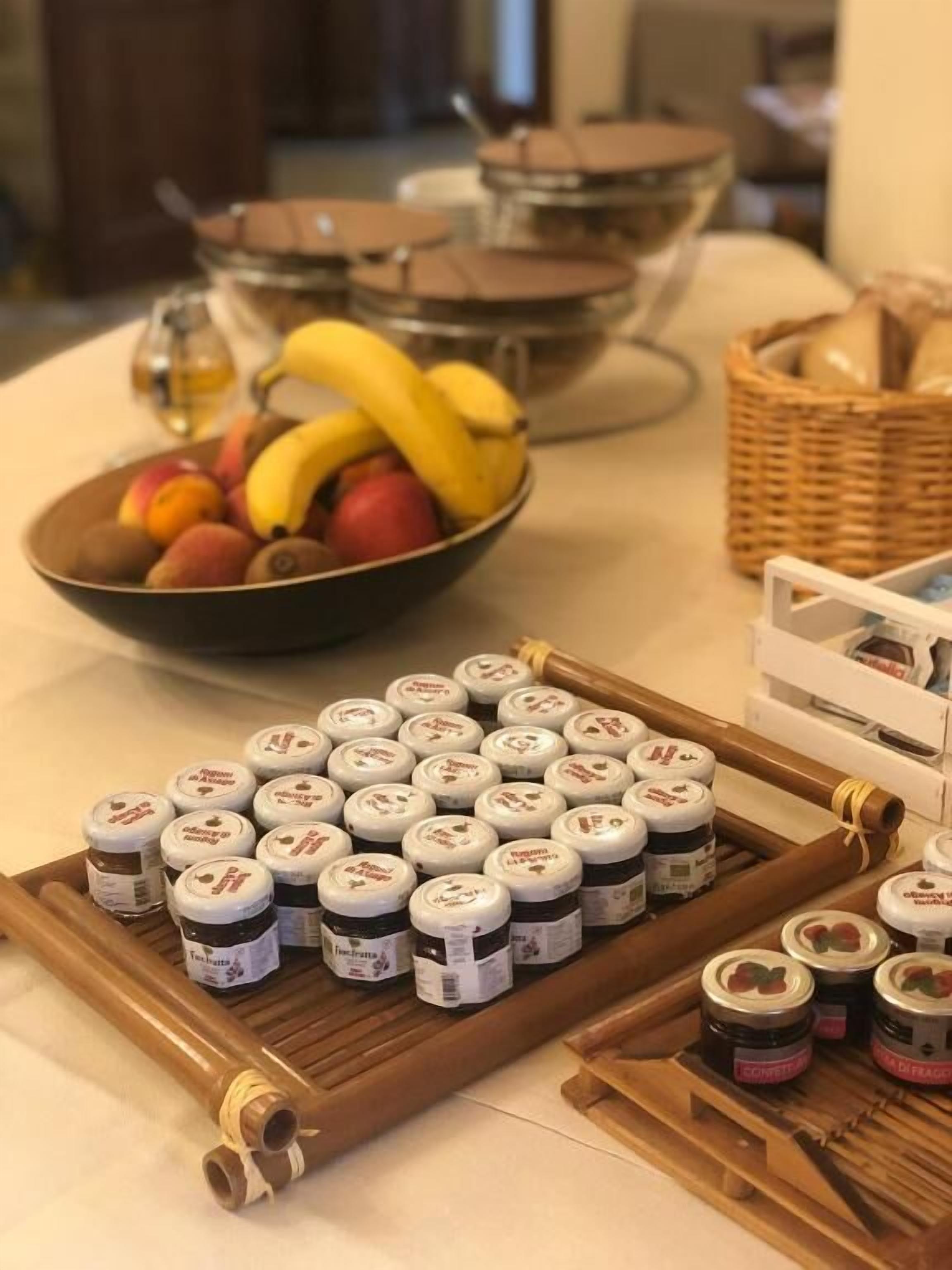 A table with jars of jam, a bowl of fruit, and a basket of bread.