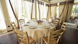 Een ronde eettafel voor zes personen, gedekt met witte tafelkleden en houten stoelen met beklede zitplaatsen.