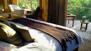 A bedroom with a large bed, a bathtub, and a balcony with a table and chairs. - Miombo Safari Camp (Dete)