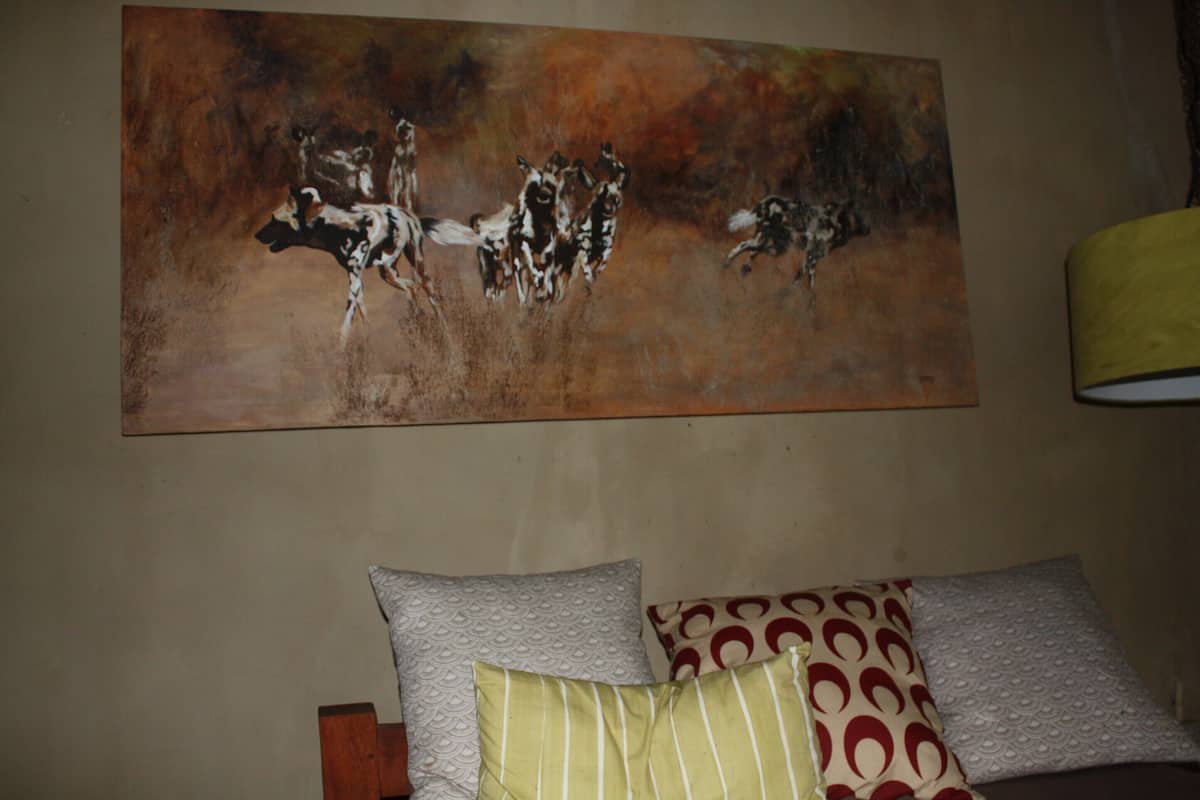 A room with a large abstract painting on the wall, a bed with patterned pillows, and a lamp on the side.