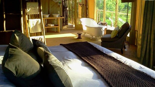 A bedroom with a large bed, a bathtub, and a chair. - Miombo Safari Camp (Dete)