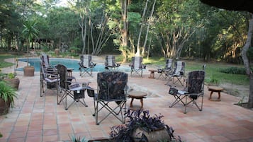 An outdoor patio with a pool, surrounded by trees and potted plants.