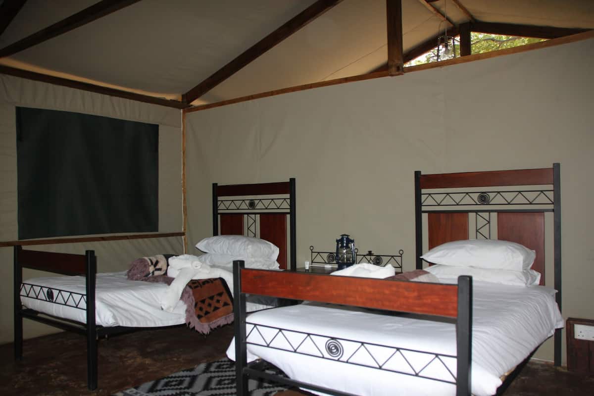 A room with two beds, each with a wooden frame and white bedding. There is a small table between the beds with a lantern on it.