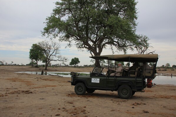 A safari vehicle parked near a water body with trees in the background.