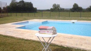 A swimming pool with a tiled deck, surrounded by a grassy area and a metal fence. - Chambres d'Hotes du Guillot (Sainte-Solange)