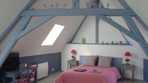 A bedroom with a sloped ceiling, a bed with a red patterned bedspread, two bedside tables with lamps, a desk with a chair, and a radiator. - Chambres d'Hotes du Guillot (Sainte-Solange)