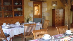 A dining area with wooden tables and chairs, a cabinet with dishes, and a striped tablecloth. - Chambres d'Hotes du Guillot (Sainte-Solange)