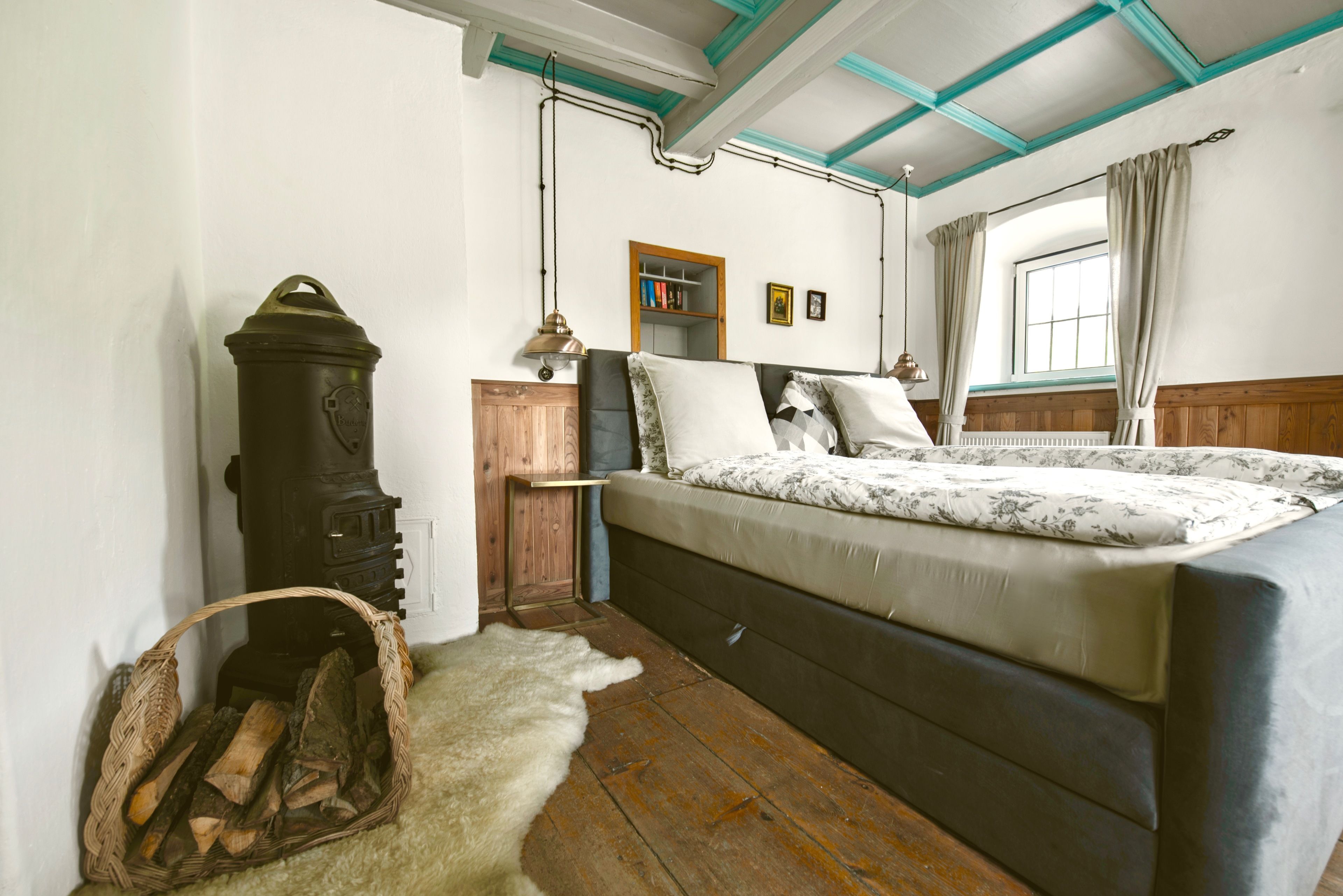 Ein Schlafzimmer mit einem Bett, einem Holzschrank, einer Lampe, einem Heizkörper und einem Fenster mit Vorhängen.