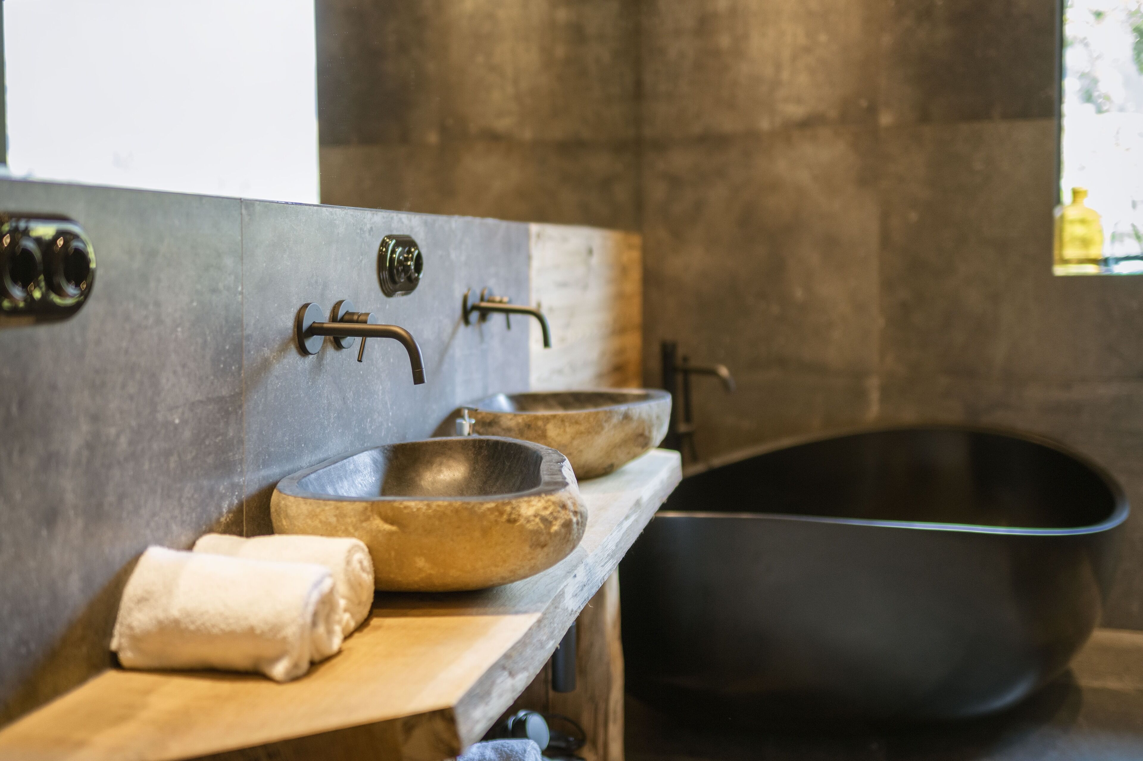 A modern bathroom with a freestanding bathtub, a wooden vanity with three bowls, and a towel on the counter.