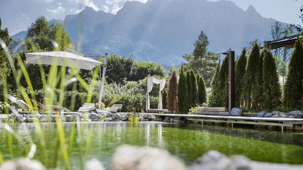 A serene outdoor pool area with lounge chairs and a canopy, surrounded by lush greenery and mountains in the background. - Bauernhaus-Schloss Wagrain (Ebbs)