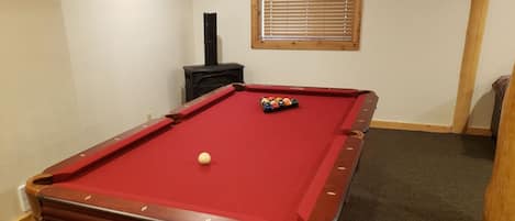 Ein Billardtisch mit roter Spielunterlage und weißem Spielball, umgeben von einem Teppichboden.